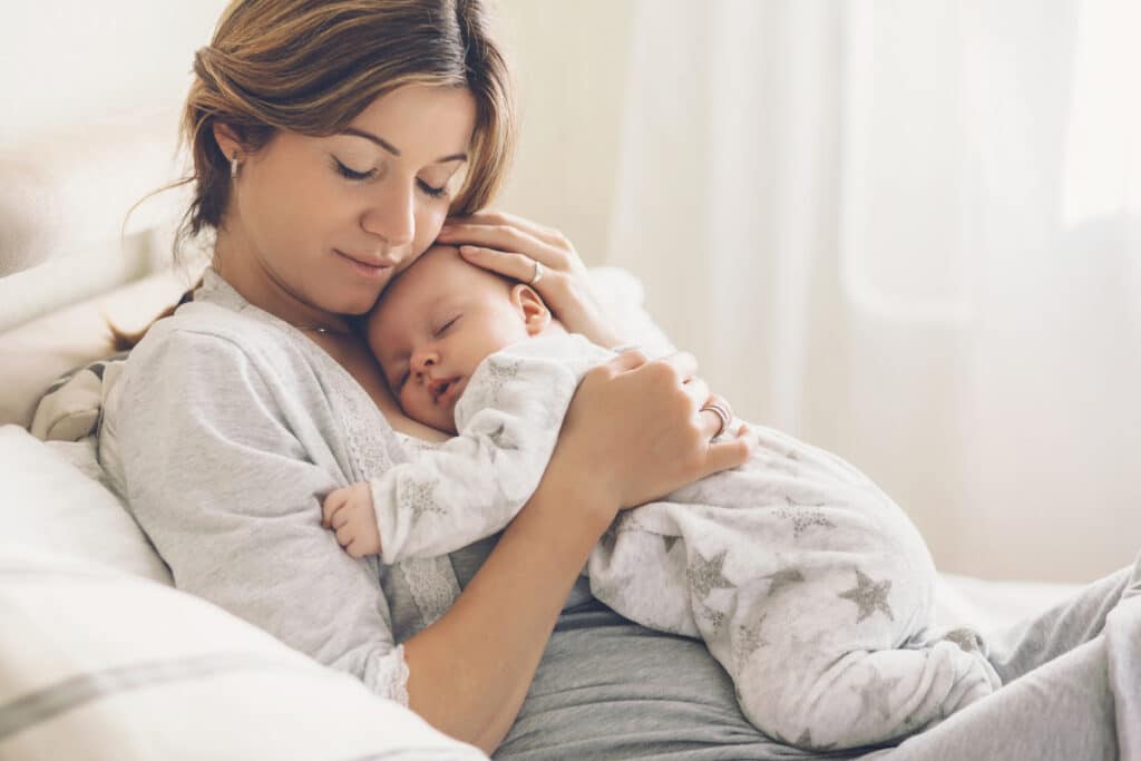 A Mother Holding Her Sleeping Baby, Highlighting The Support Sleep Consultants Provide To Help Families Establish Peaceful Sleep Routines.